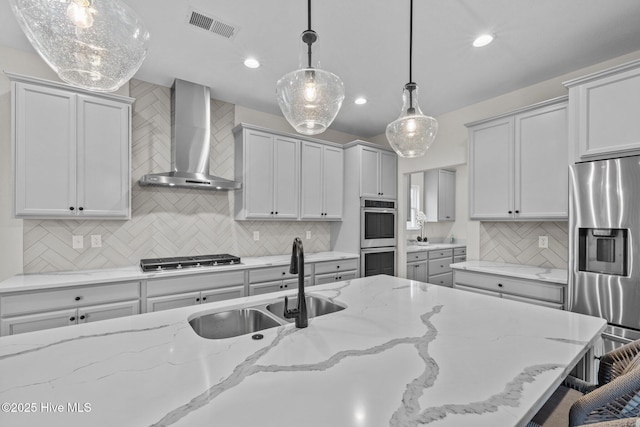 kitchen featuring light stone countertops, hanging light fixtures, wall chimney exhaust hood, and stainless steel appliances