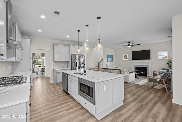 kitchen with an island with sink, stainless steel appliances, tasteful backsplash, decorative light fixtures, and sink