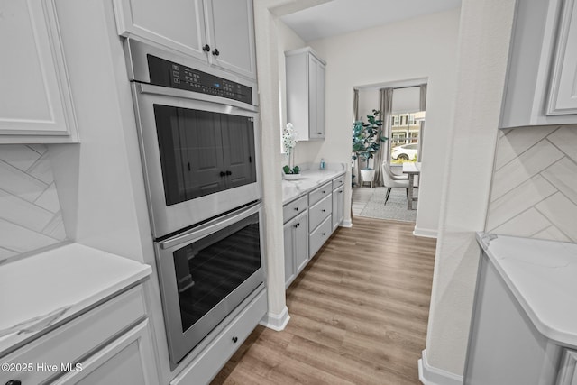 kitchen with white cabinetry, double oven, backsplash, light wood-type flooring, and light stone counters