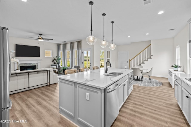 kitchen featuring a center island with sink, sink, light stone countertops, stainless steel appliances, and white cabinets