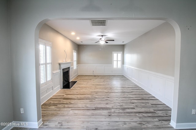 unfurnished living room featuring ceiling fan, a wainscoted wall, wood finished floors, a fireplace with flush hearth, and visible vents