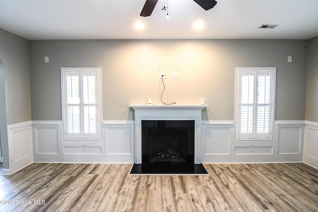 unfurnished living room featuring a fireplace with flush hearth, a wainscoted wall, visible vents, and wood finished floors