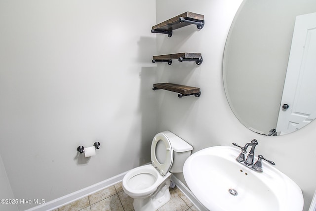 half bath featuring tile patterned flooring, toilet, a sink, and baseboards