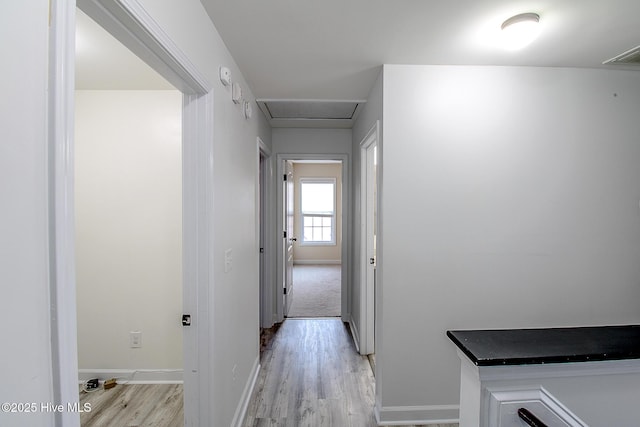 hallway with visible vents, light wood-style flooring, attic access, and baseboards