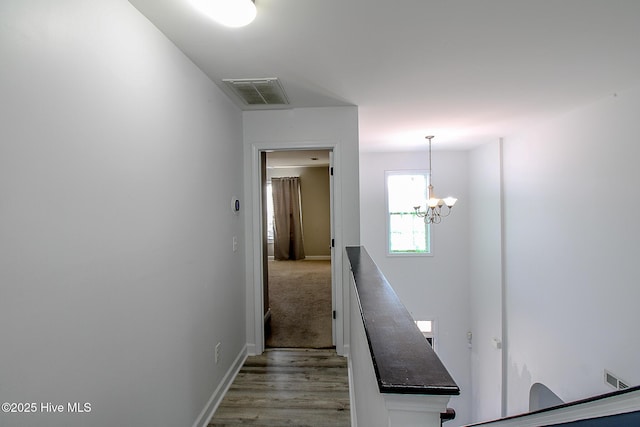 corridor with visible vents, a notable chandelier, baseboards, and wood finished floors