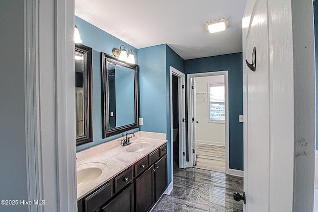 bathroom with marble finish floor, double vanity, a sink, and baseboards