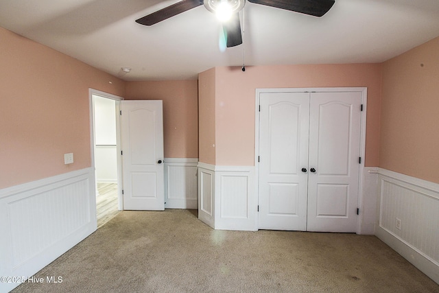 unfurnished bedroom with carpet, a closet, wainscoting, and ceiling fan