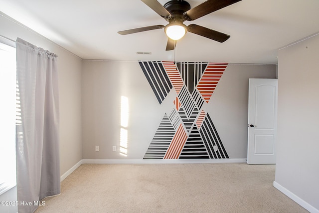 carpeted spare room with ceiling fan, visible vents, and baseboards