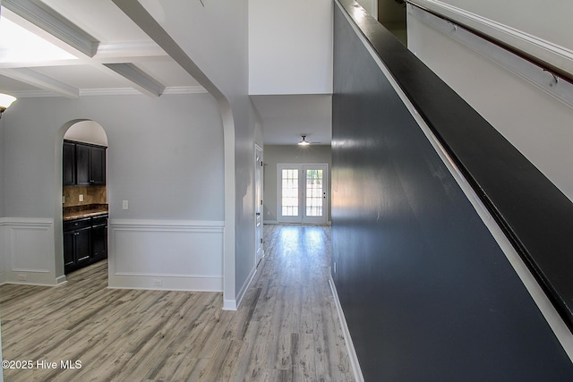 corridor featuring arched walkways, coffered ceiling, wainscoting, light wood-type flooring, and beam ceiling