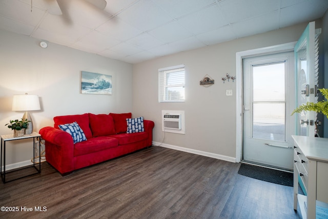 living room featuring a drop ceiling, dark wood-type flooring, and an AC wall unit