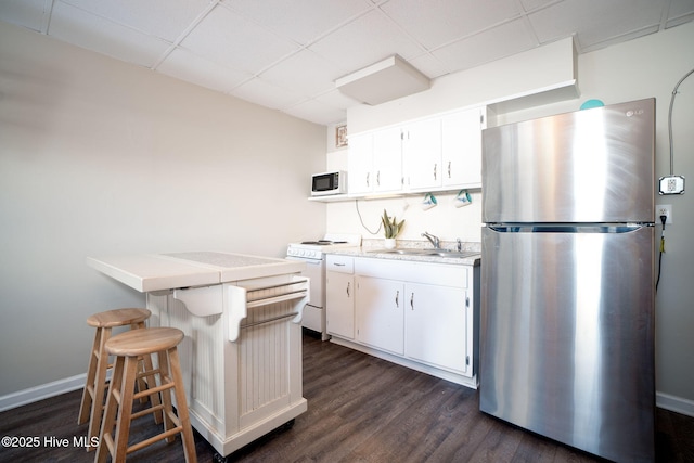 kitchen with a paneled ceiling, white electric range, stainless steel refrigerator, white cabinetry, and dark wood-type flooring