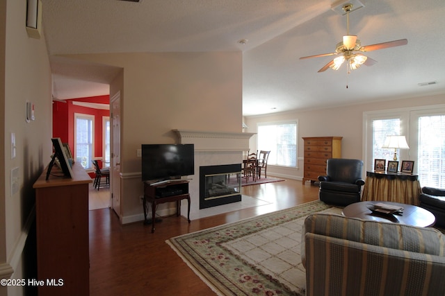 living room with dark wood-type flooring, vaulted ceiling, ceiling fan, and a premium fireplace