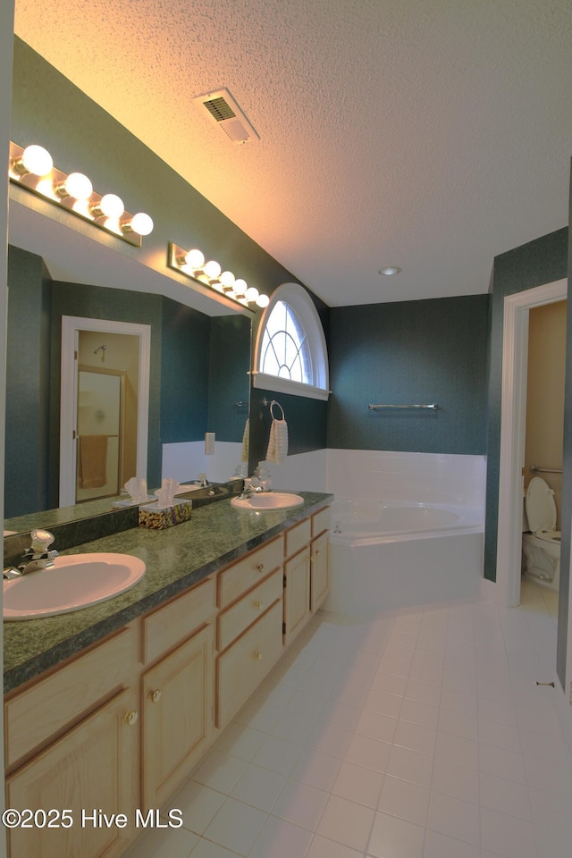 bathroom with a textured ceiling, tile patterned floors, vanity, toilet, and a bathing tub