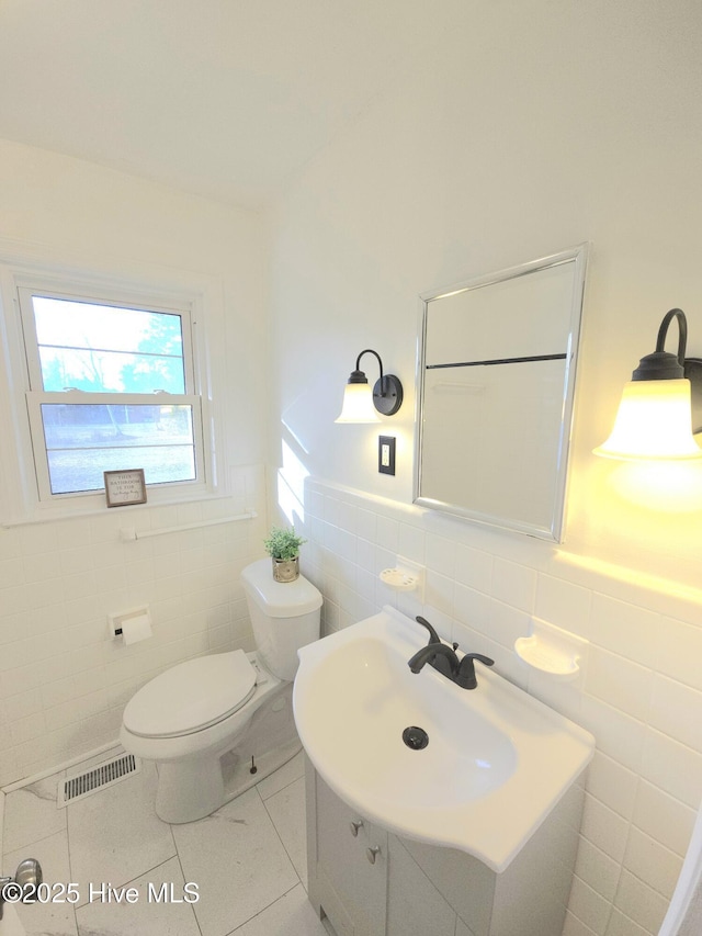 bathroom with toilet, vanity, tile patterned floors, and tile walls