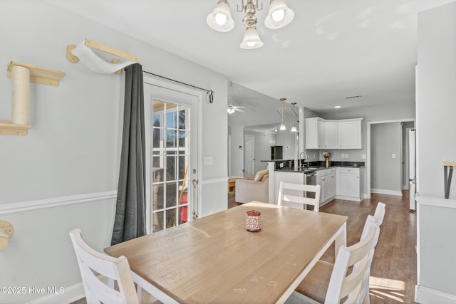 dining space featuring ceiling fan with notable chandelier, sink, and wood-type flooring