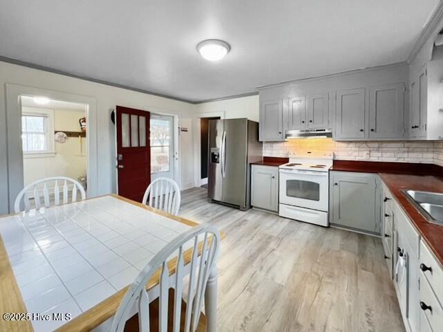 kitchen with stainless steel fridge, tile counters, range hood, white electric stove, and light hardwood / wood-style flooring