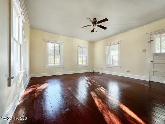 empty room featuring ceiling fan, a healthy amount of sunlight, and dark wood-type flooring