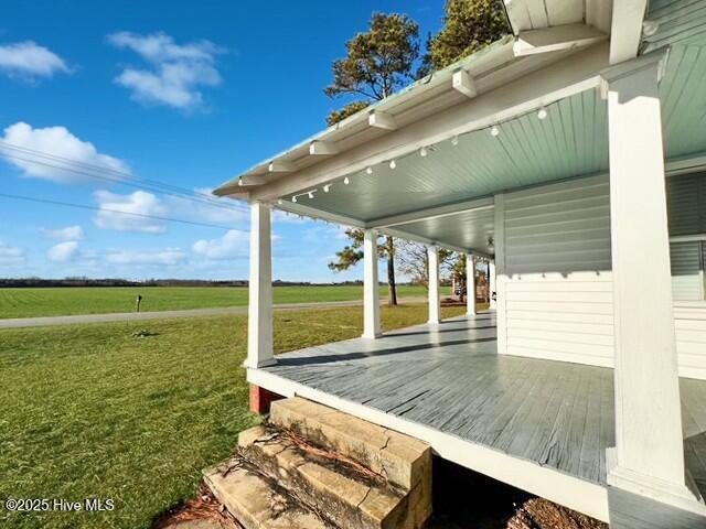 wooden deck with covered porch, a rural view, and a lawn