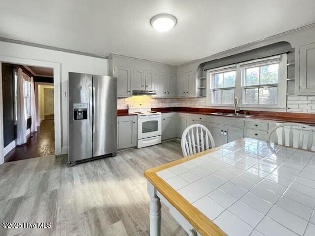 kitchen featuring tasteful backsplash, stainless steel refrigerator with ice dispenser, white electric range, sink, and tile counters