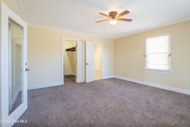 unfurnished bedroom with a textured ceiling, a walk in closet, carpet floors, a closet, and ceiling fan