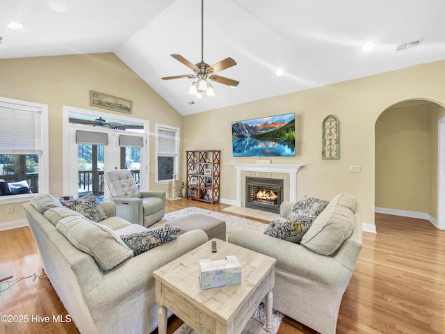 living room with a tile fireplace, high vaulted ceiling, ceiling fan, and light hardwood / wood-style flooring