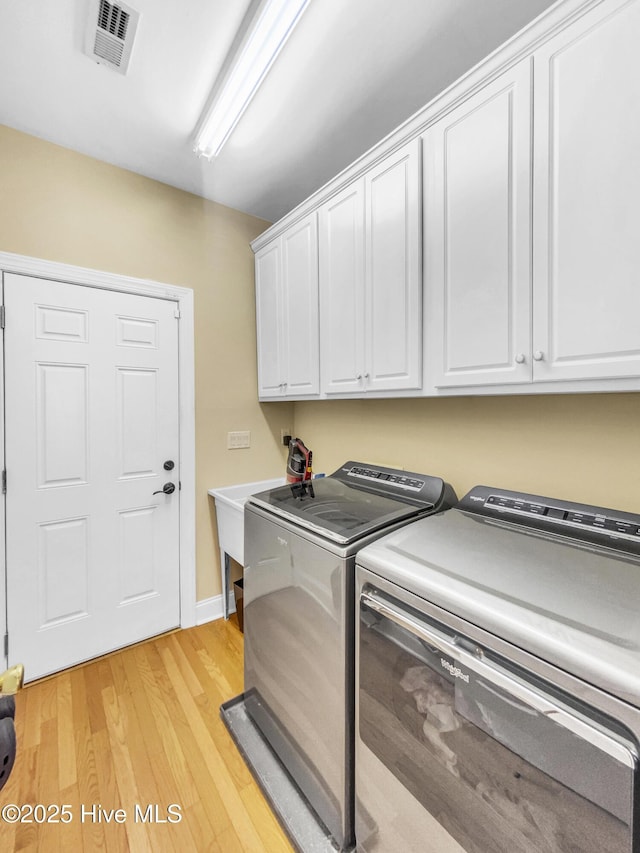 clothes washing area with cabinets, light hardwood / wood-style floors, and washing machine and dryer