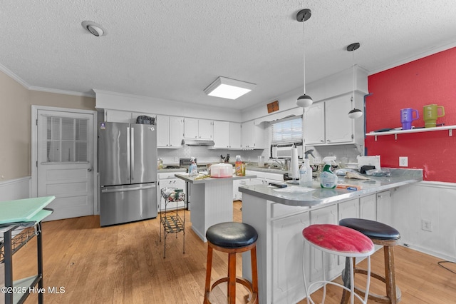 kitchen with a breakfast bar area, stainless steel refrigerator, white cabinetry, hanging light fixtures, and kitchen peninsula