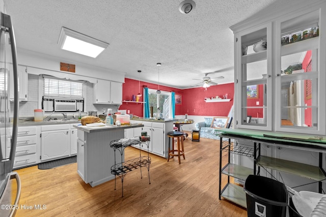 kitchen with a breakfast bar, white cabinetry, decorative light fixtures, light hardwood / wood-style flooring, and a kitchen island