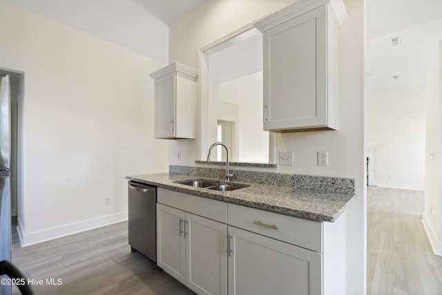 kitchen featuring light stone counters, stainless steel dishwasher, sink, and light wood-type flooring