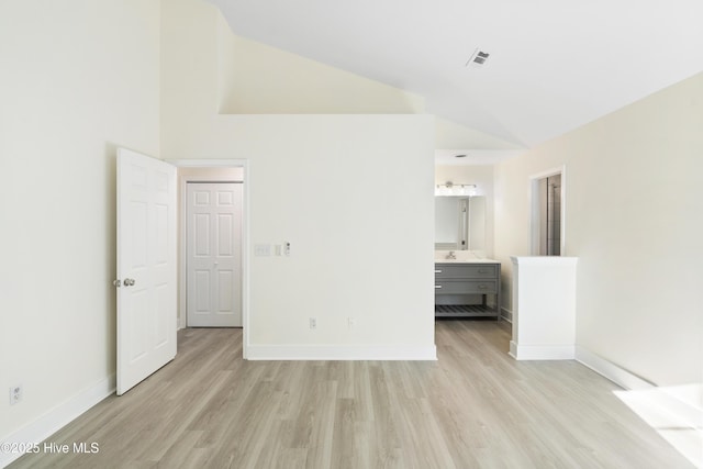 unfurnished bedroom featuring sink, ensuite bath, high vaulted ceiling, and light hardwood / wood-style floors