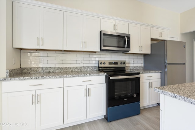 kitchen with appliances with stainless steel finishes, tasteful backsplash, white cabinets, light stone counters, and light hardwood / wood-style flooring