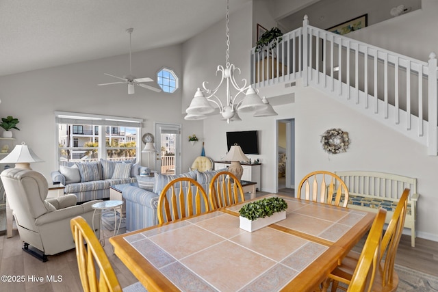 dining room with ceiling fan with notable chandelier, wood-type flooring, and a towering ceiling