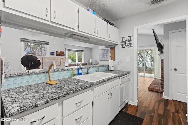 kitchen featuring open floor plan, dark wood-style flooring, white dishwasher, white cabinetry, and a sink