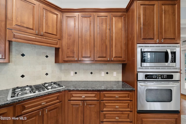 kitchen with crown molding, appliances with stainless steel finishes, dark stone counters, and backsplash