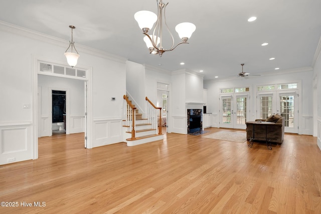 unfurnished living room featuring an inviting chandelier, ornamental molding, french doors, and light wood-type flooring