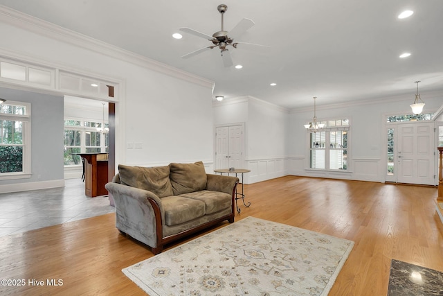 living room featuring ornamental molding, ceiling fan with notable chandelier, and light wood-type flooring