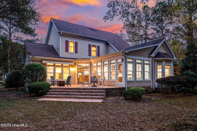 back house at dusk featuring a sunroom and a patio