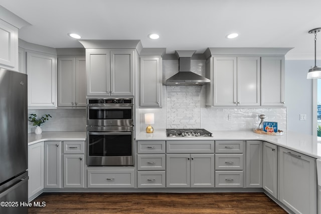 kitchen featuring appliances with stainless steel finishes, gray cabinetry, hanging light fixtures, tasteful backsplash, and wall chimney exhaust hood