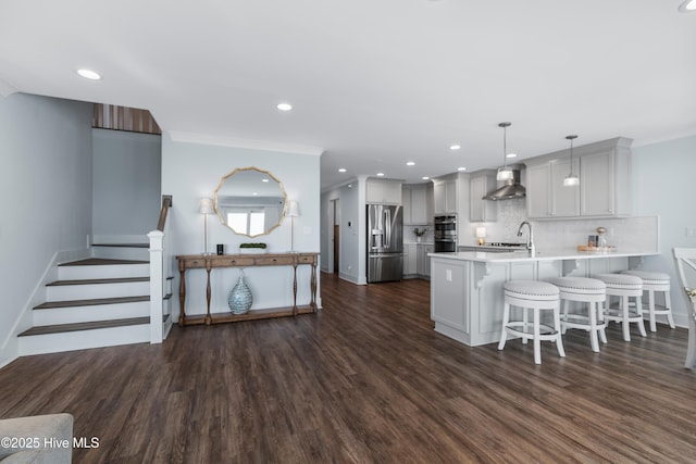 kitchen with wall chimney range hood, a breakfast bar area, appliances with stainless steel finishes, hanging light fixtures, and kitchen peninsula