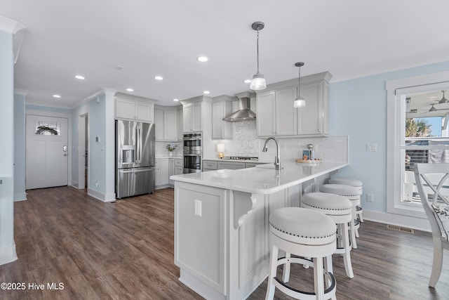 kitchen featuring a breakfast bar area, decorative light fixtures, appliances with stainless steel finishes, kitchen peninsula, and wall chimney range hood