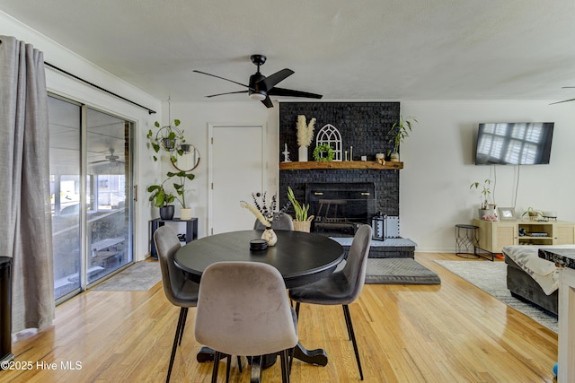 dining space featuring a brick fireplace, a textured ceiling, ceiling fan, and light wood-type flooring