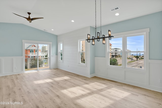 unfurnished dining area with ceiling fan with notable chandelier, lofted ceiling, and light wood-type flooring