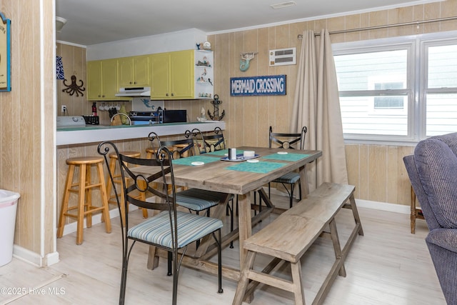 dining room with crown molding, a wall mounted air conditioner, light hardwood / wood-style floors, and wood walls