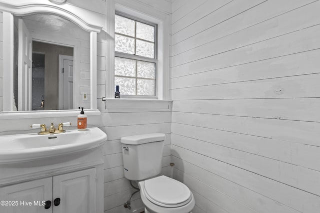 bathroom featuring toilet, vanity, and wood walls