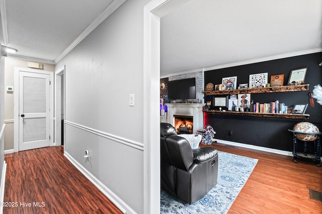 living room featuring wood-type flooring, a large fireplace, a textured ceiling, and ornamental molding