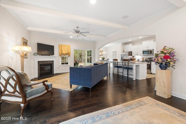 living room featuring ornamental molding, ceiling fan, beam ceiling, and dark hardwood / wood-style floors