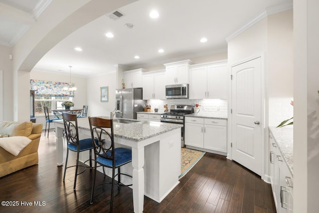 kitchen featuring pendant lighting, appliances with stainless steel finishes, white cabinets, a breakfast bar, and an island with sink