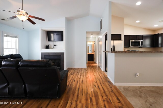 kitchen with ceiling fan, stainless steel fridge, dark hardwood / wood-style flooring, and dark stone counters