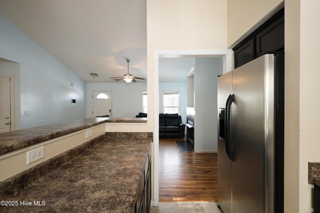 kitchen with stainless steel refrigerator with ice dispenser, dark countertops, a ceiling fan, open floor plan, and wood finished floors