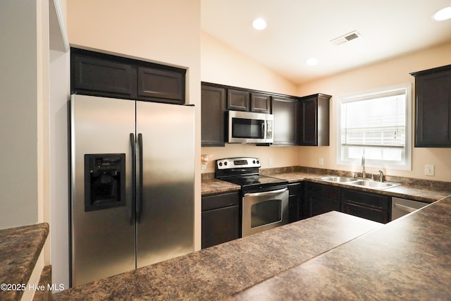 kitchen featuring lofted ceiling, stainless steel appliances, a sink, visible vents, and dark countertops